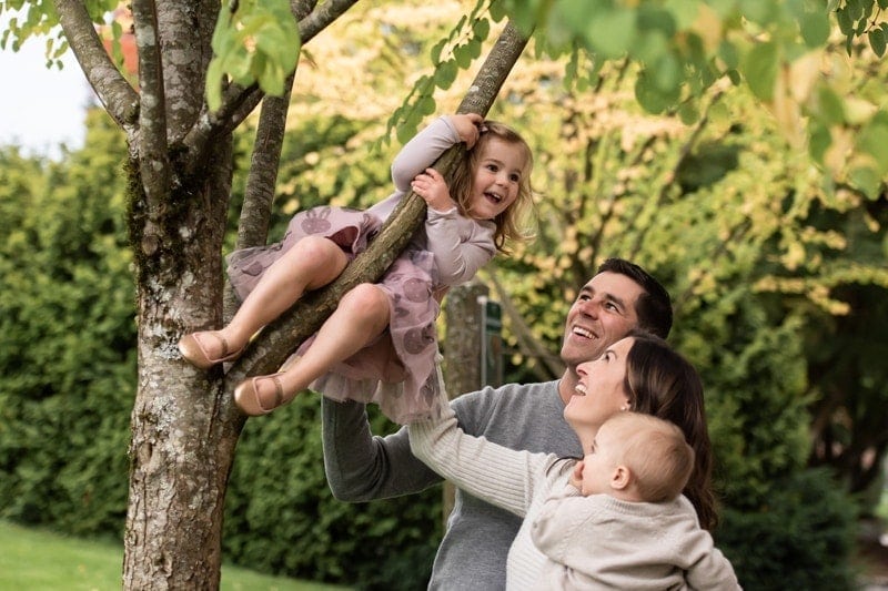 Family Photography, little girl climbing up in tree next to her mom and dad